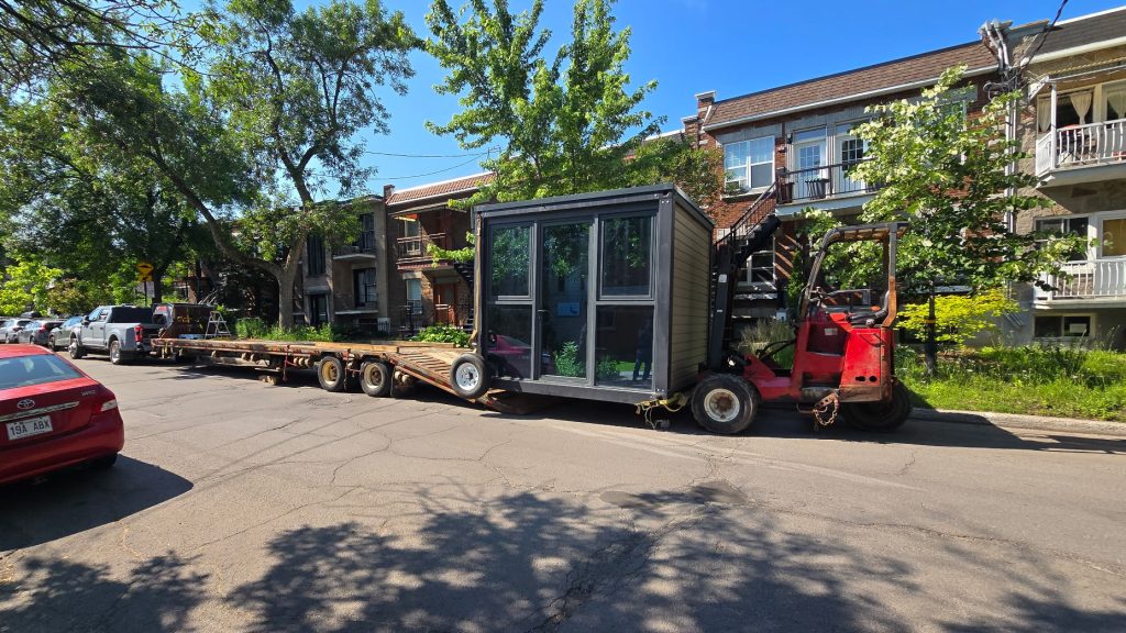 Livraison d’un cabanon avec un chariot élévateur rouge dans une rue résidentielle.