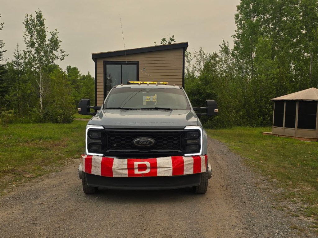 Front view of a Transport JKM truck carrying a shed, with oversize load signage.