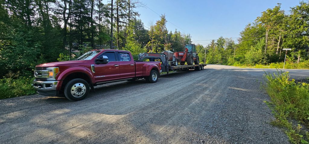 A red Transport JKM pickup truck and equipment trailer on a wooded road.
