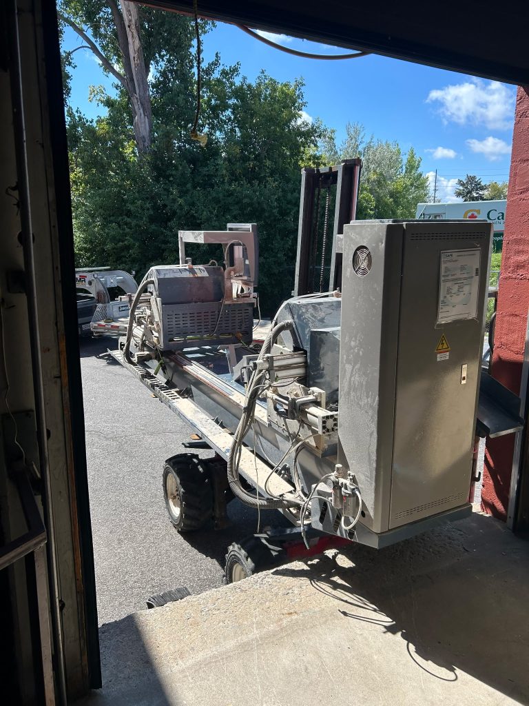 An industrial machine being moved out of a workshop with a forklift.