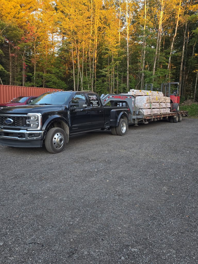 A black pickup truck and materials trailer in front of trees in autumn.