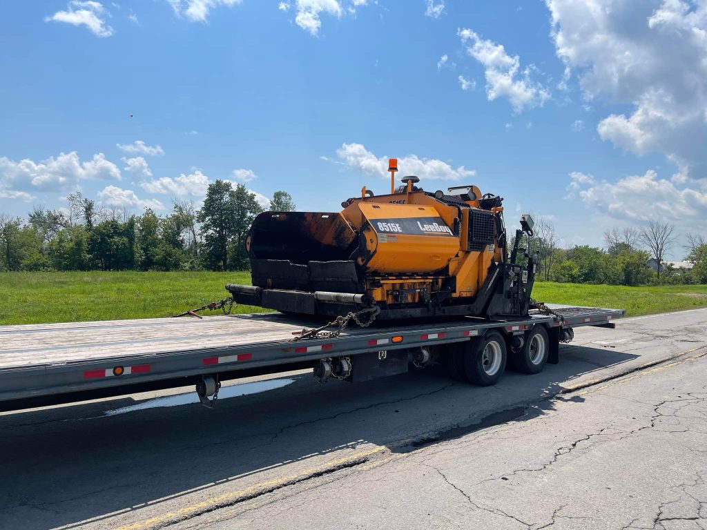 Paveuse orange sur une remorque à plateforme Transport JKM.