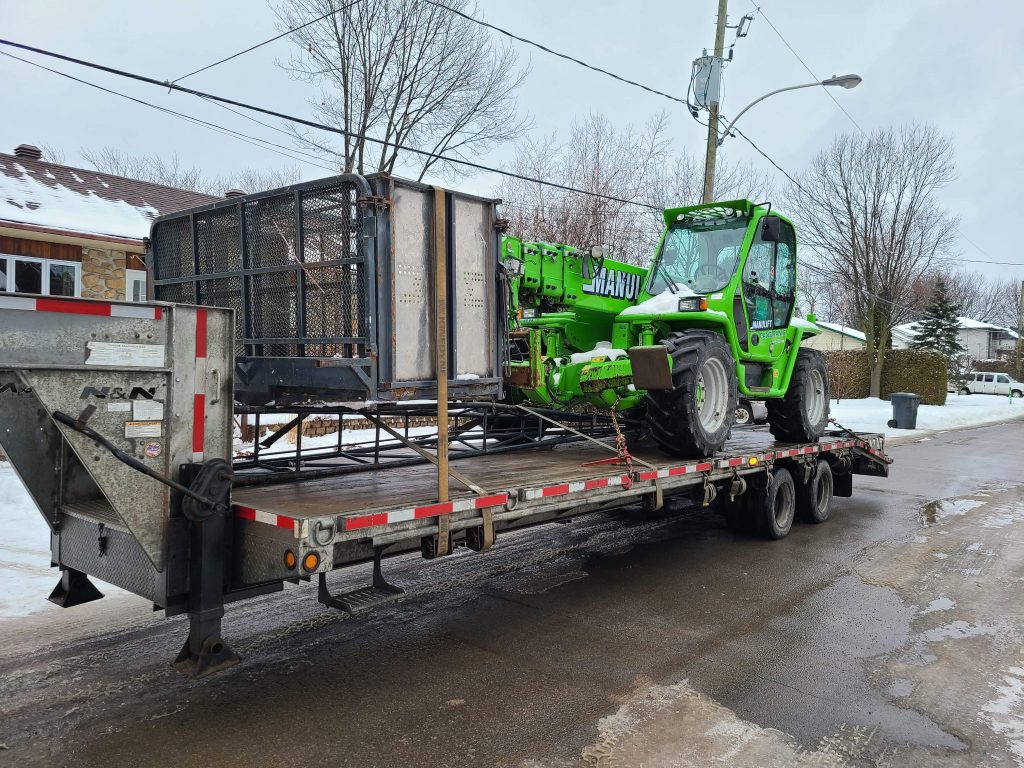 A green telehandler on a trailer in winter.