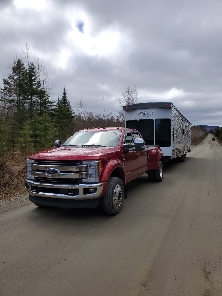 A red Transport JKM pickup truck towing a travel trailer on a road.