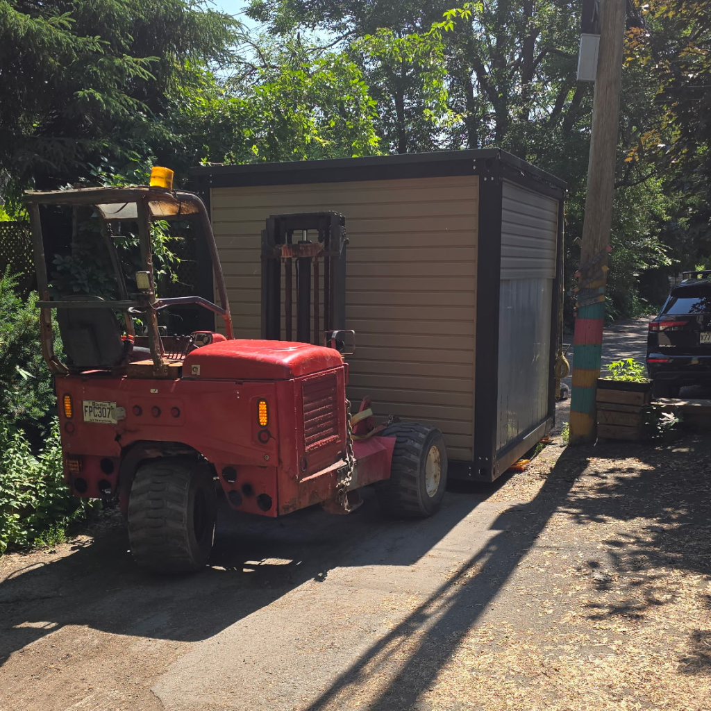 Chariot élévateur rouge déplaçant un cabanon sur une allée.