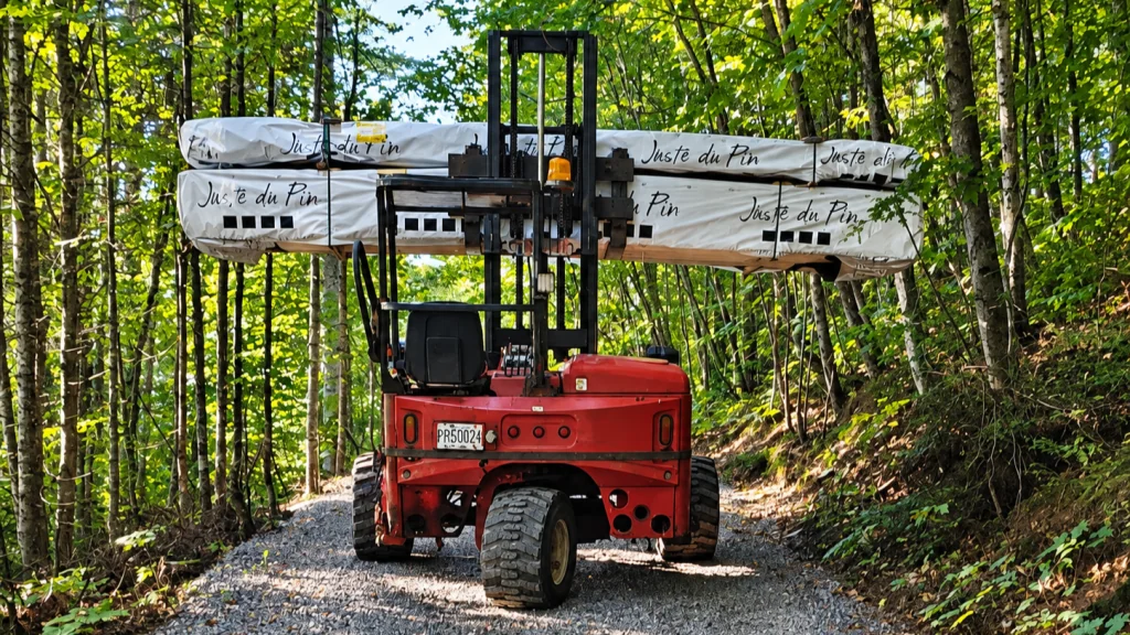 A forklift carrying a long wrapped load along a wooded access road.